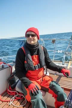 Skilled young man in red hat steering a sailboat with wooden tiller on the op Stock Photos