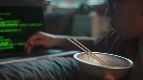 Skilled Young Programmer Writing Code on Laptop while Eating Noodles Stock Footage 290872592