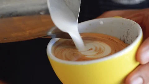 A skillful barista pouring a rosetta pattern latte art in a yellow coffee Stock Footage 111809639