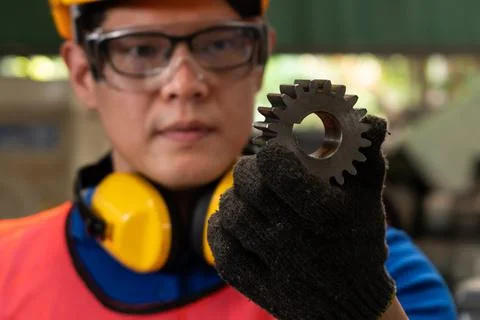 Skillful factory worker looking at machine part in workshop Stock Photos