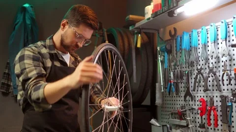 Skillful handsome focused mechanic fixing bike wheel with tools standing in Stock Footage 232492289