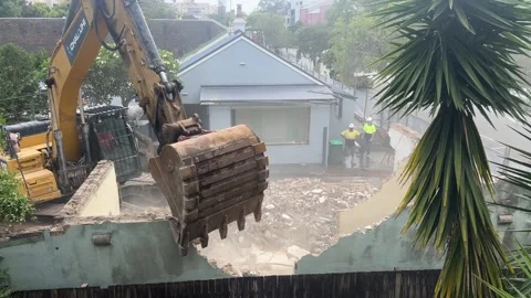 A skillful operator uses digger to knock down wall avoiding a fence 4K Stock Footage 327050188