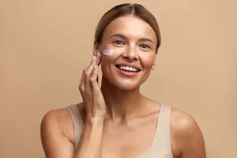 Skin Care Woman Applying Cream on Cheek. Beautiful Smiling Girl Putting Cream Stock Photos