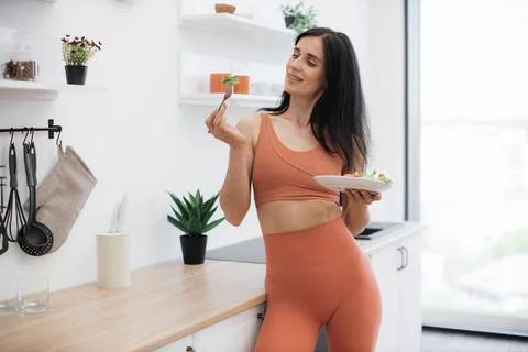 Skinny lady leaning on kitchen surface with salad in hands 库存照片