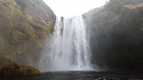 Skogafoss waterfall plunging down a high cliff surrounded by green mossy rock Stock Footage 339303953
