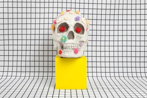 A skull covered with multiple plastic flowers on a white squared tile pattern Stock Photos