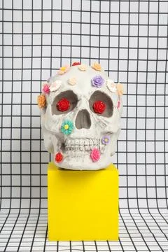 A skull covered with multiple plastic flowers on a white squared tile pattern Stock Photos