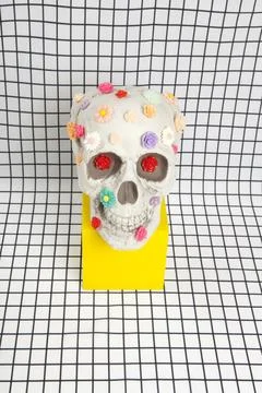 A skull covered with multiple plastic flowers on a white squared tile pattern Stock Photos