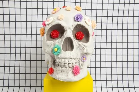 A skull covered with multiple plastic flowers on a white squared tile pattern Stock Photos