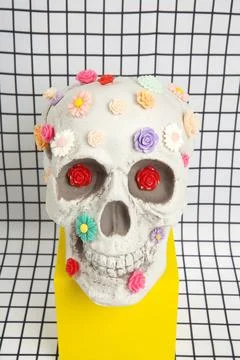 A skull covered with multiple plastic flowers on a white squared tile pattern Stock Photos