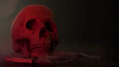 A skull in a red glow stands on a table with syringes Stock Footage 156796079