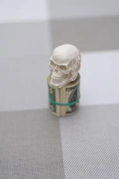 A skull standing on a bundle of money, twisted into a bundle Stock Photos