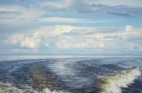 Sky with clouds over the water. a trace of a boat on the water surface, waves Stock Photos
