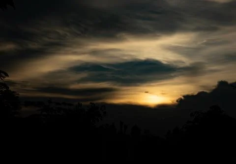 The sky is dark and cloudy with a sun in the background Stock Photos