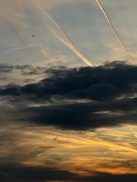 Sky at dusk with layered clouds, visible aircraft contrails Stock Photos