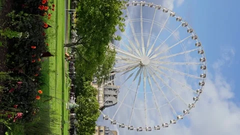 Sky-high ferris wheel surrounded by water, clouds, plants, and electric blue sky Stock-Footage 267159711
