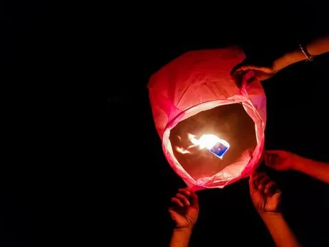 Sky lantern lighting by a pair of hands holding the paper hot air balloon in  Stock Photos