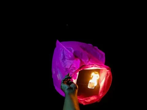 Sky lantern lighting by a pair of hands holding the paper hot air balloon in  Stock Photos