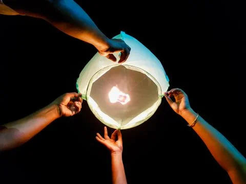 Sky lantern lighting by a pair of hands holding the paper hot air balloon in  Stock Photos