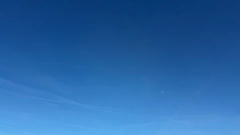 Sky showing a clear blue expanse with visible airplane contrail, a distant moon Stock Footage 333699855