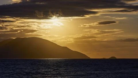 The sky shows a dramatic sunset with dark clouds and an island on the horizon, Stock Photos