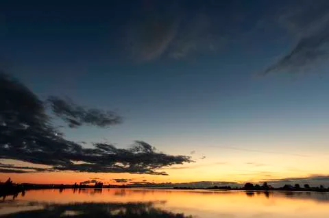 Sky with thick gray clouds reflecting in the river, a scarlet sunset over the Stock Photos