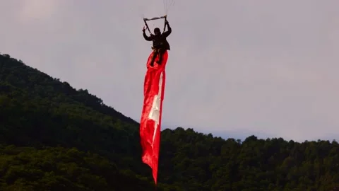 Skydiver Flying with a Hanging Swiss Flag and Mountain in a Sunny Day Stock-Footage 196810285