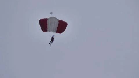 Skydiver opens a red and white flag as he lands between the on a very cloudy day Stock Footage 158181091