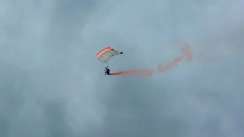Skydiver with Orange Smoke Trail Performing Aerial Stunts Vidéo 345485240