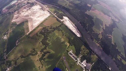 Skydiver parachuting in sky over field, woods. Extreme activity. Adrenaline Stockbeeldmateriaal 69965906