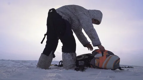 A skydiver in winter clothes is standing on the top of the hill and is wrapping Stock Footage 88100790