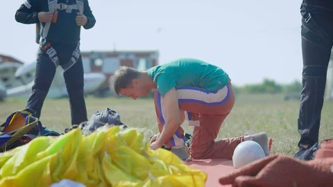 Skydivers are preparing for flight on ground, man is checking equipment in Stock Footage 95099929
