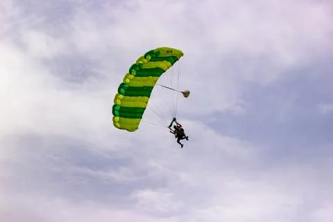 Skydivers gliding down with a green parachute in an overcast sky. Stock Photos