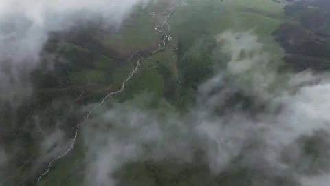 Skydiving view from clouds to green mountain valley with winding stream in Stock Footage 312380765