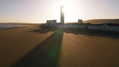 Skyscraper casting a long shadow over a beach at sunrise 스톡 동영상 336771672