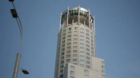 Skyscraper in the form of pillar, round large building against blue sky. View of Stock Footage 244492744