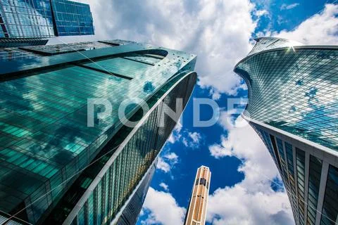 Skyscrapers against blue sky with white fluffy clouds reflected on glass of b Stock Photos