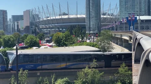 Skytrain passing underneath a viaduct with background of BC Place on Sunny Day Stock Footage 281058425