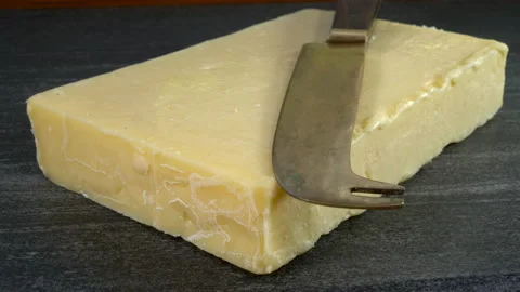 Slab of fresh cheddar cheese on a marble board with a knife on top. Video stock 157446097