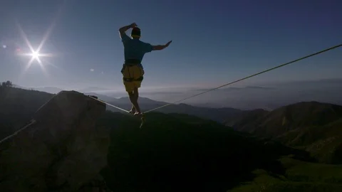 Slackliner crosses a valley in front of a setting sun in slow motion Stock Footage 90818458