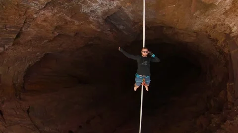 Slackliner is lying on the tightrope stretched over the massive pit, 4k Stock Footage 133557700