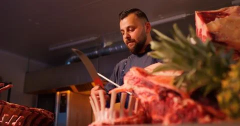 Slaughterhouse worker sharpens knife on professional sharpener. Stock Photos
