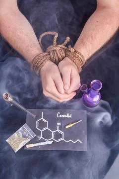 Slave of cannabis concept. Bound male hands with bong and smoking pipe. Stock Photos
