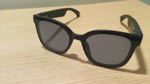 Sleek black smart glasses with integrated audio technology resting on a light Video stock 318610889