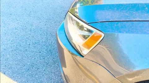 Sleek car headlight reflecting sunlight, shimmering on asphalt, a modern Video stock 318317298