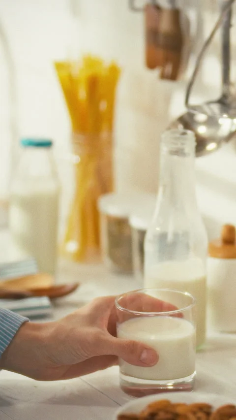 In a sleek modern kitchen a womans hand lifts a glass of milk as she assembl Stock Footage 331795040