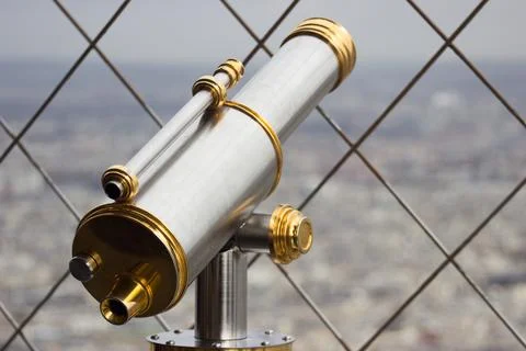 Sleek telescope peers through a chainlink fence over the city Fotos Stock