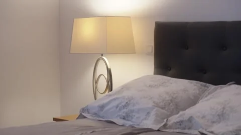 Sleeping area, with a close-up of the bedside table and a stylish designer lamp Stock Footage 334803365