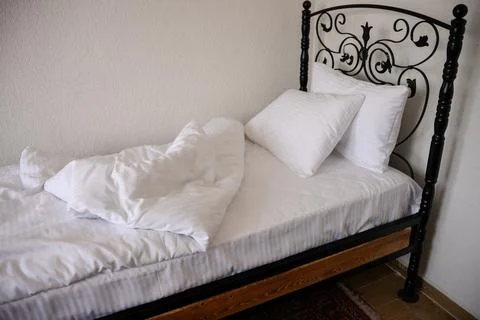 Sleeping area with rumpled blankets, sheets on carved iron bed, bathed in Stock Photos