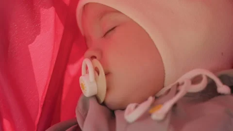Sleeping baby with pacifier in stroller, soft closeup under pink canopy, newborn Stock Footage 334621409